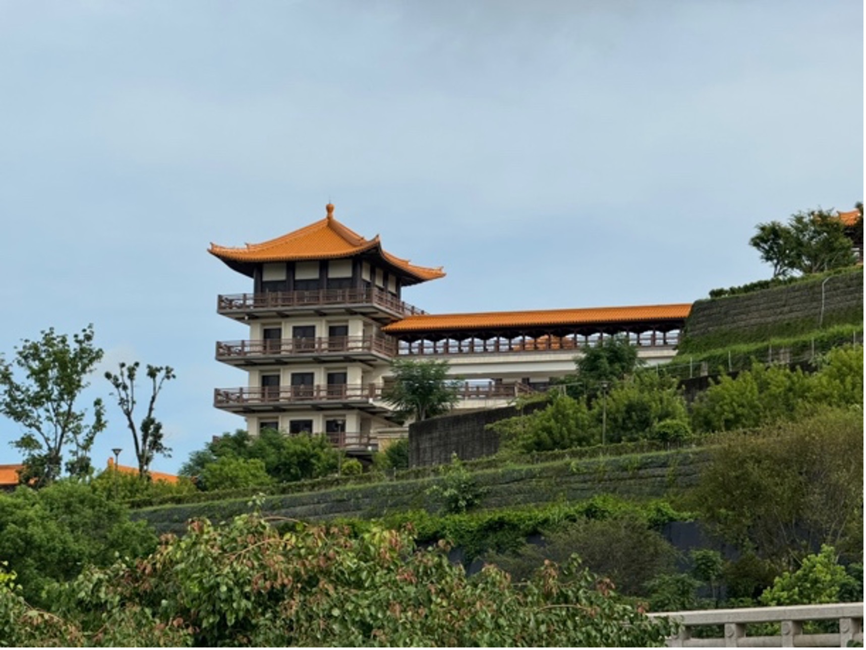 A photo of a building with deep eaves set against a tall hill with beautiful gardens.