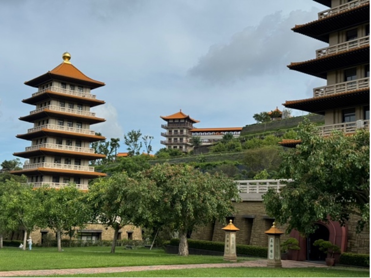 Another photo of said building, this time further away with trees in the lower half and two tall buildings with many stacked deep eaves.