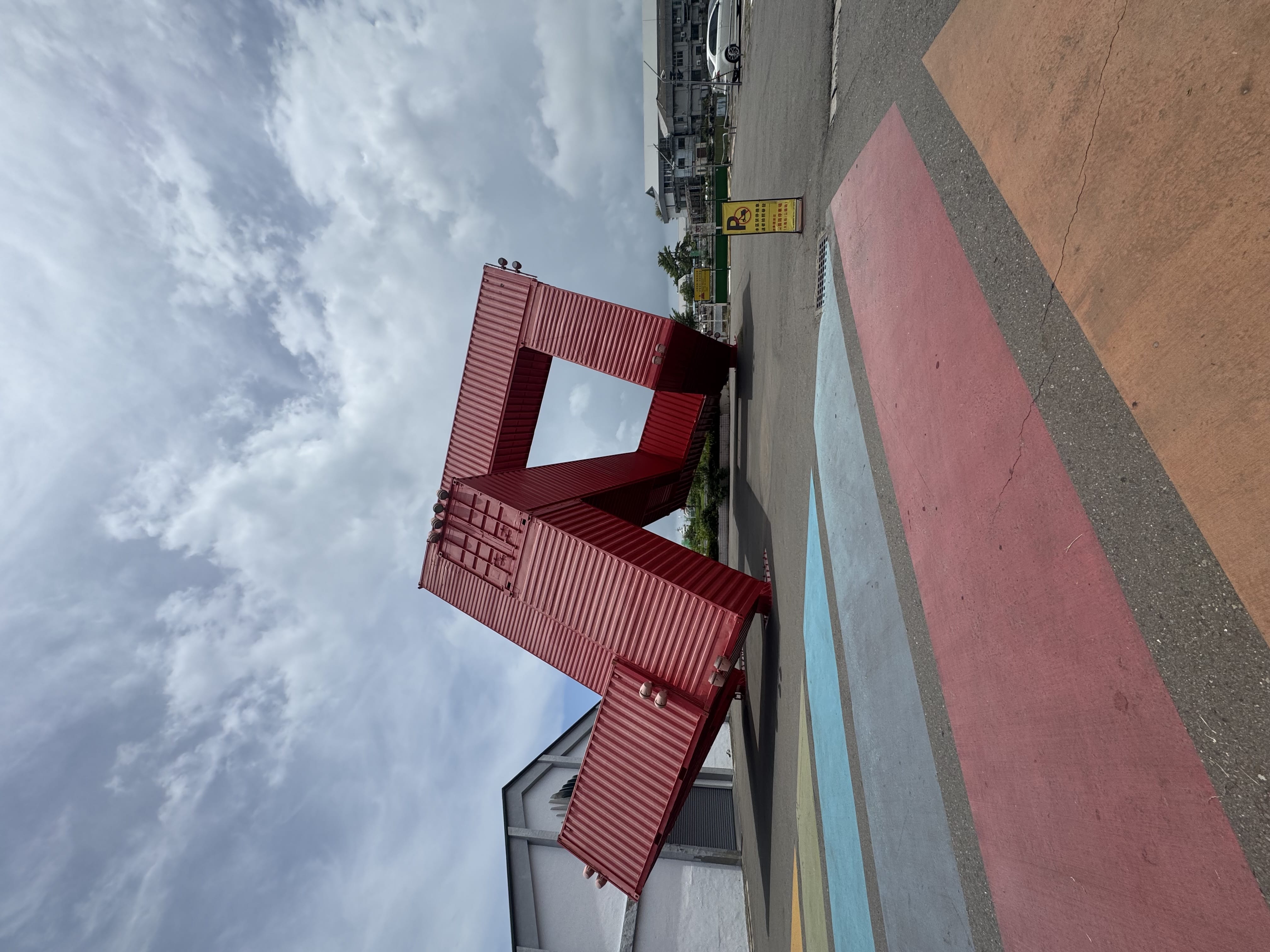 Large red sculpture made from stacked shipping containers against a cloudy sky.