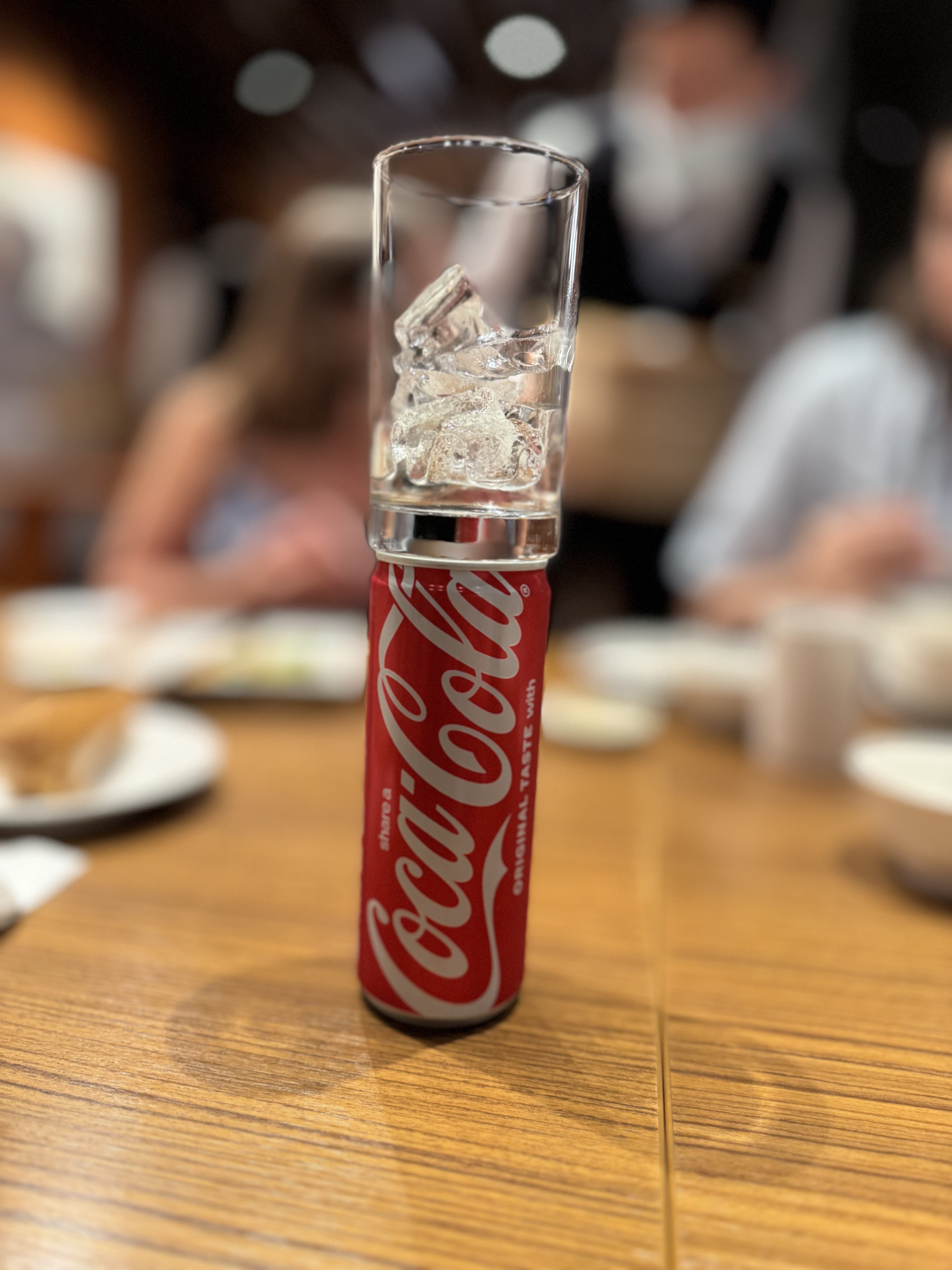 Coca-Cola can with a glass of ice set on top, on a restaurant table.