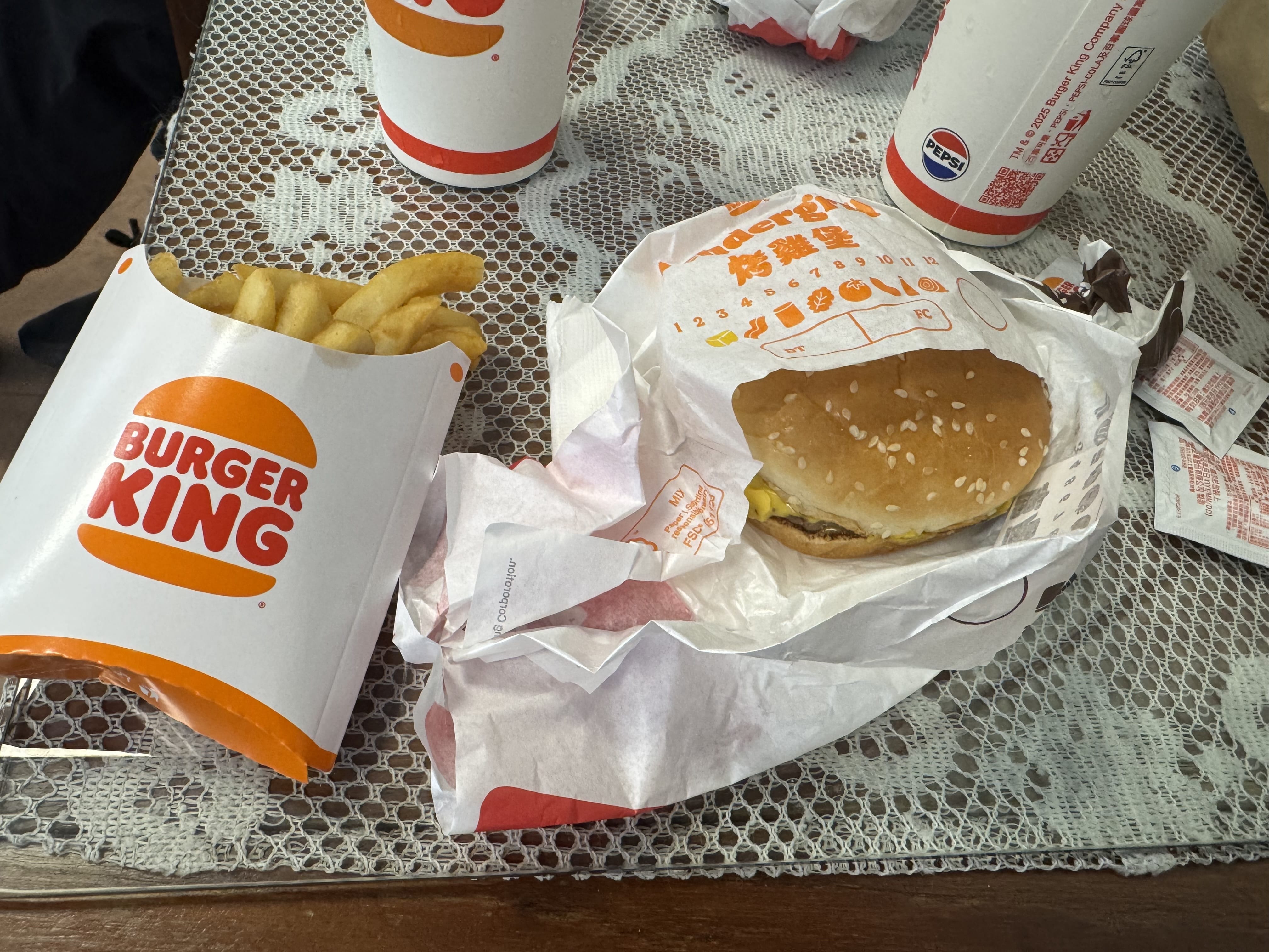 Burger King fries, a wrapped sesame-seed burger, and a drink cup on a lace tablecloth.