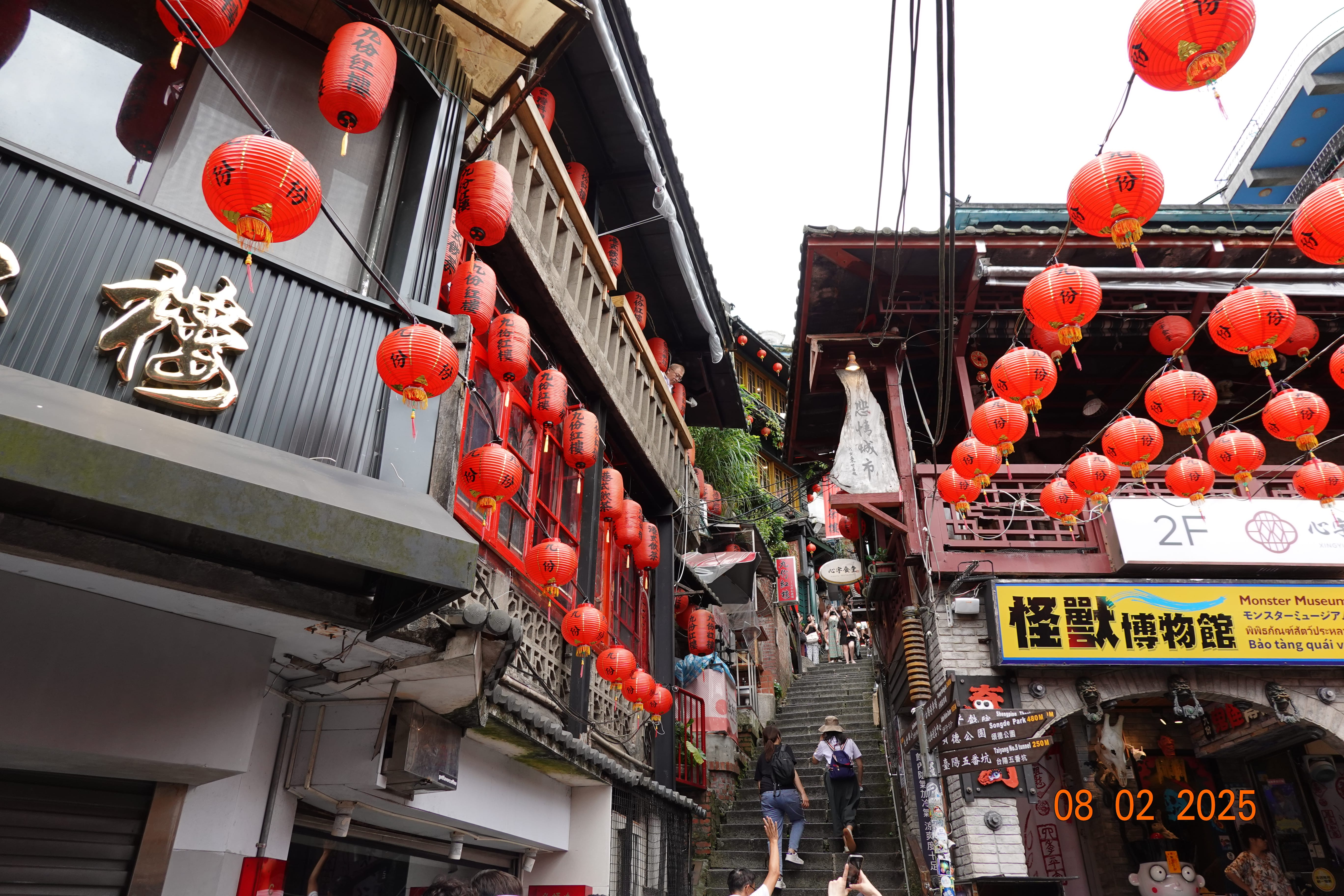 Narrow stairway alley in Jiufen lined with red lanterns and busy shops, Monster Museum sign visible; 08-02-2025.