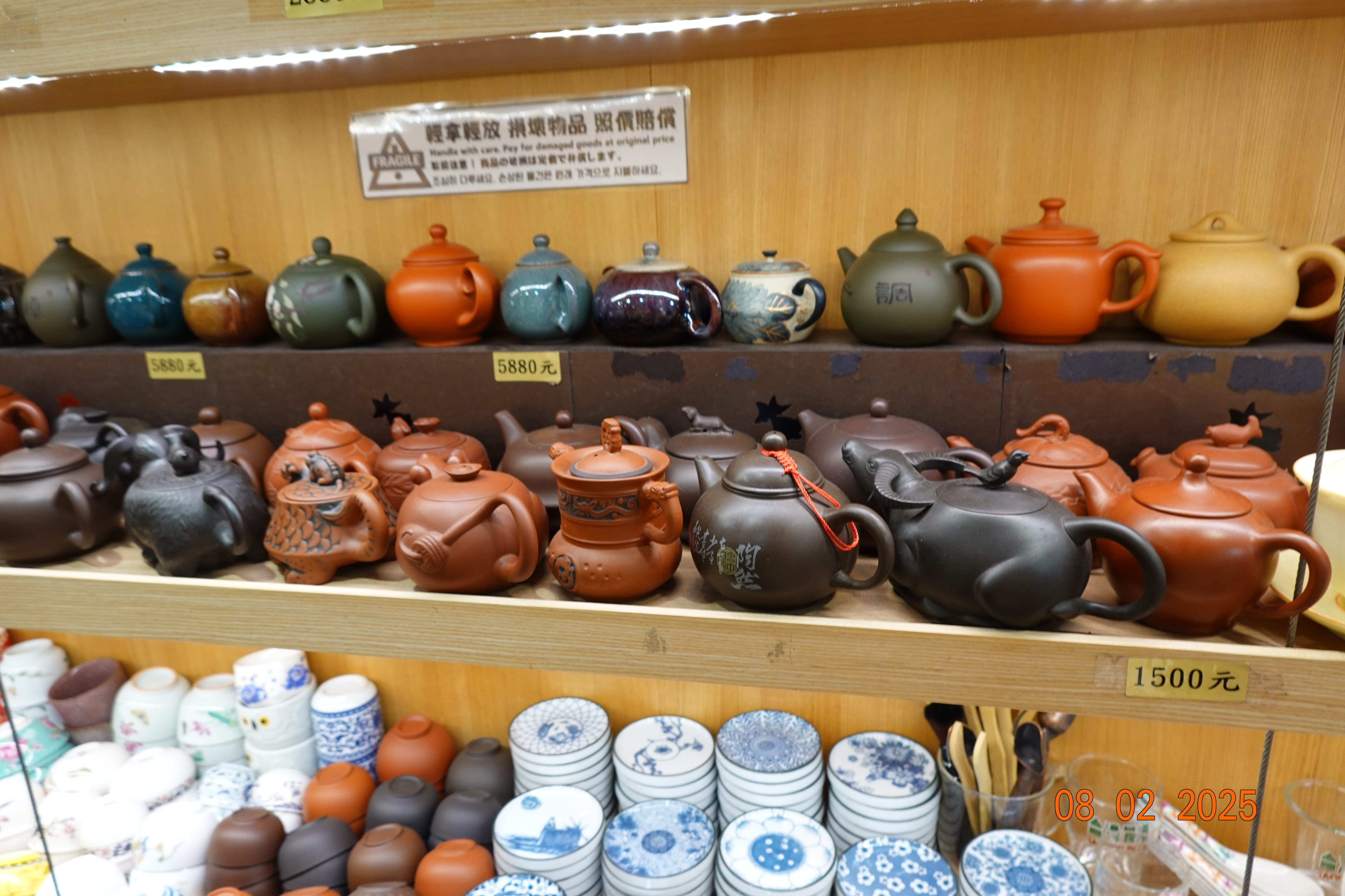 Shelves of Yixing-style clay teapots and ceramic cups in a shop, price tags shown in New Taiwan dollars; 08-02-2025.
