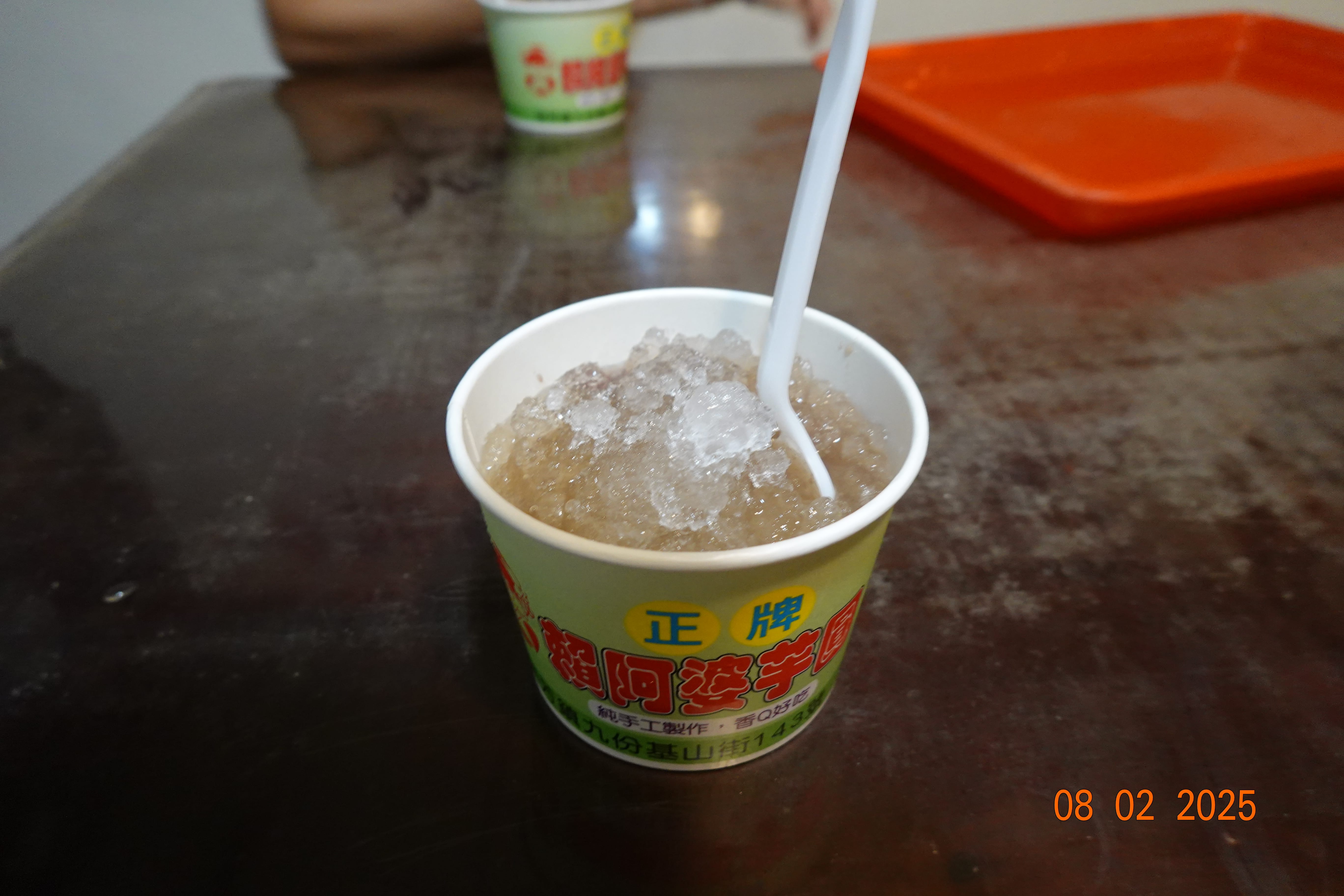 Paper cup of shaved ice dessert with a spoon on a table at a local shop; 08-02-2025.