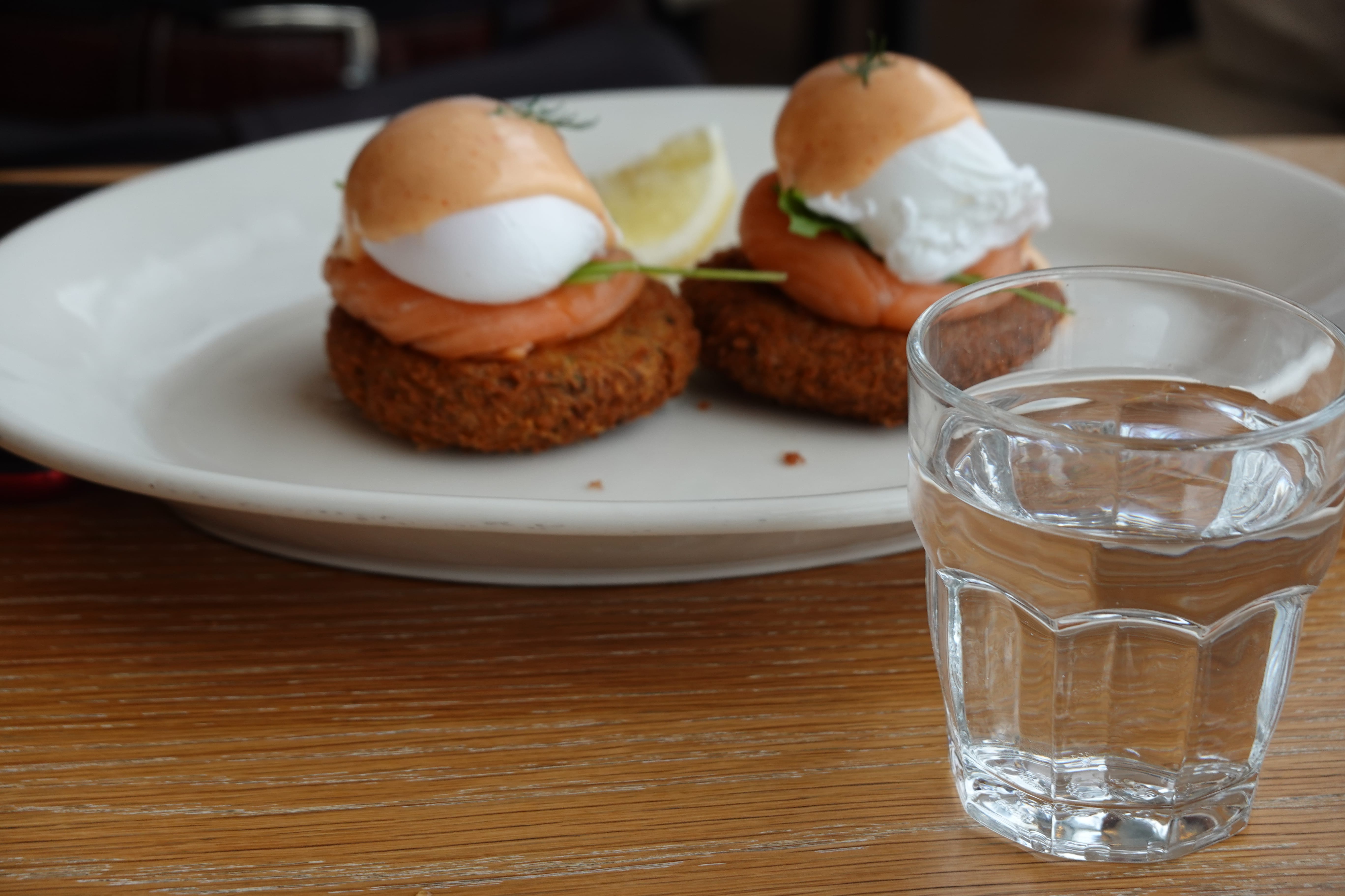 Brunch plate with two salmon eggs Benedict on crispy patties, lemon wedge, and a glass of water.